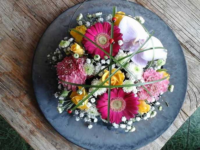 composition florale-fleurs roses blanches et jaunes présentées sur assiette et plan de travail en bois